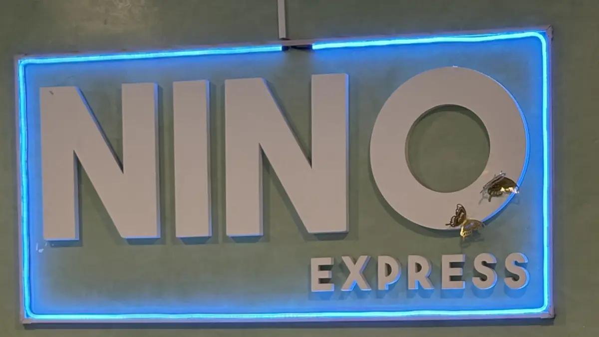 El cartel de adentro: las letras blancas de Nino Express sobre la pared verde, con luz azul alrededor